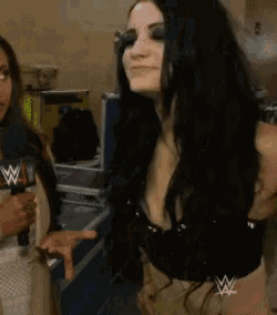 two women are standing next to each other in a room and one of them is wearing a microphone with the letters w on it .