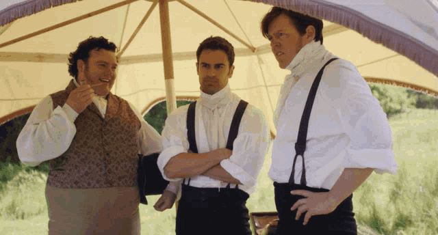 three men are standing under an umbrella and talking