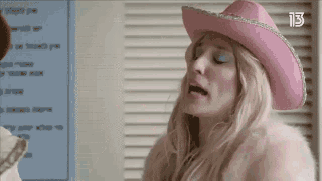 a woman wearing a pink cowboy hat and a pink fur coat is making a funny face .