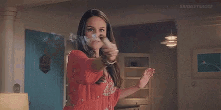 a woman in a red dress is smoking a cigarette in a living room with smoke coming out of her hands .