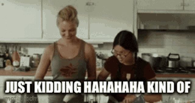 two women are standing in a kitchen with the words just kidding  hahaha kind of written above them .