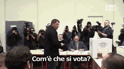 a man stands in front of a group of cameras and says " com ' e che si vota "