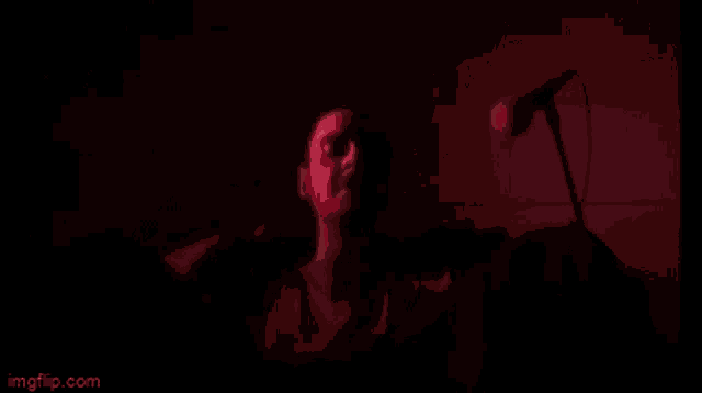 a man is singing into a microphone in a dark room while playing drums .