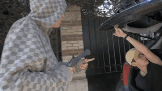 a man in a checkered hoodie is pointing a gun at another man in a yellow hat