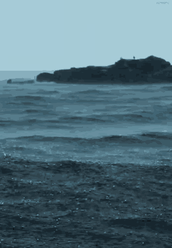 a large body of water with waves crashing on the shore and a small island in the distance .