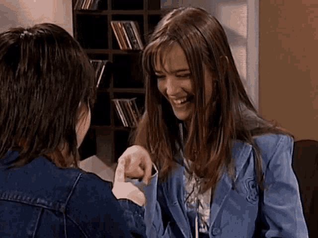 a woman in a blue jacket is laughing with another woman in a denim jacket .