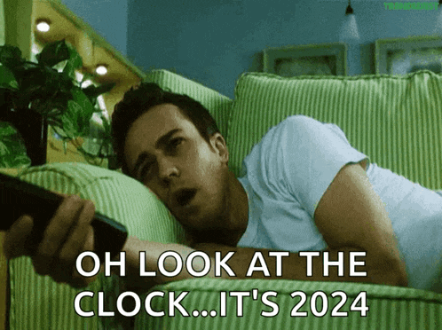 a man is laying on a couch holding a remote control with the words oh look at the clock it 's 2024