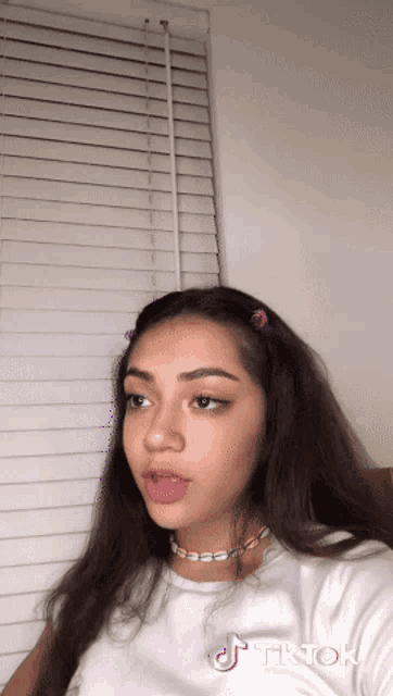 a girl wearing a white t-shirt and a necklace has a tiktok logo on her face