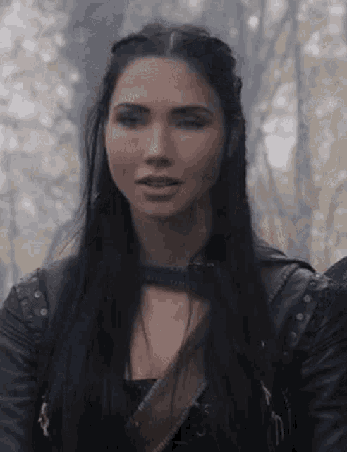 a woman with long black hair is wearing a leather jacket and a choker around her neck .