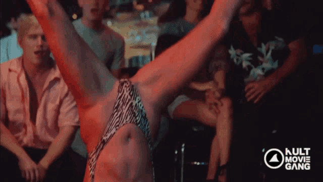 a woman in a zebra print bikini is dancing in front of a crowd and the words kult movie gang are visible in the corner