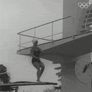 a woman in a bathing suit is standing on a diving board in front of an olympic clock