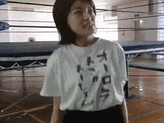 a woman wearing a white t-shirt with chinese writing on it stands in front of a wrestling ring