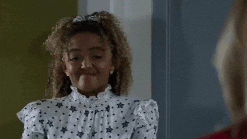 a woman with curly hair is wearing a white dress with stars on it and a ponytail .