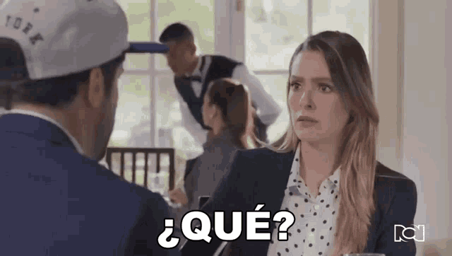 a man and a woman are sitting at a table and the woman says que