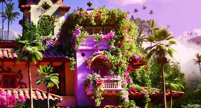 a building with a balcony covered in flowers and palm trees in the background