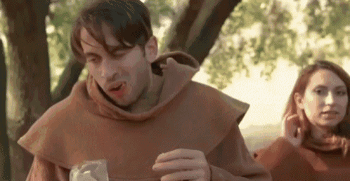 a man dressed as a monk is holding a glass of wine while a woman looks on .