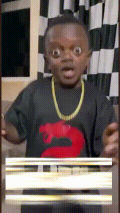 a young boy wearing a black shirt with a red s on it and a gold chain around his neck