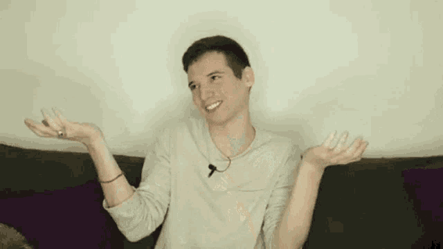 a young man is sitting on a couch with his hands outstretched and laughing .