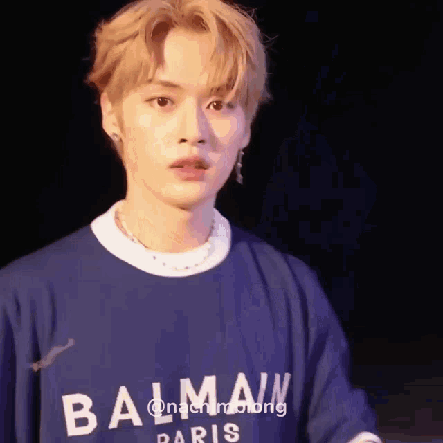 a young man wearing a blue balmain t-shirt is standing in front of a black background .