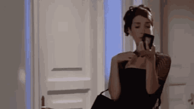 a woman in a black dress is looking at herself in the mirror .