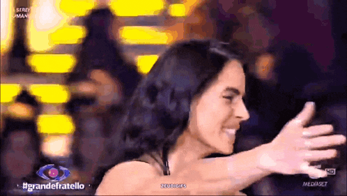 a woman is hugging another woman in front of a sign that says grandefratello on it
