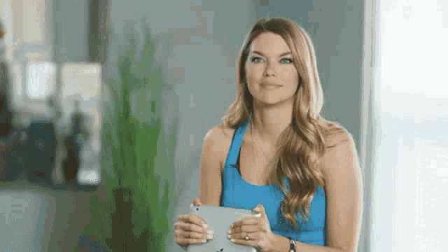 a woman in a blue tank top is holding a tablet computer .