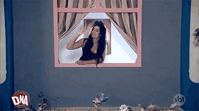 a woman is waving from a window in a room with flowers .