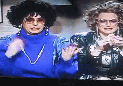 a woman in a blue turtleneck and sunglasses stands next to another woman in a black jacket