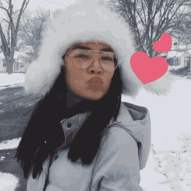a woman wearing a white hat and glasses blows a kiss in the snow