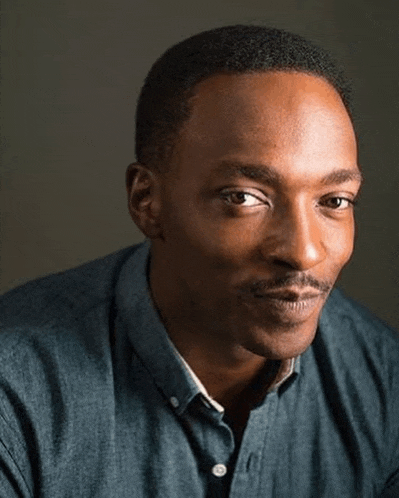 a close up of a man wearing a blue shirt and looking at the camera .