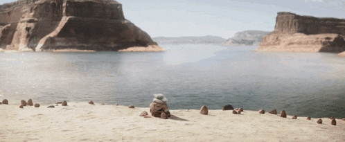 a cartoon character sits on a sandy beach near a body of water