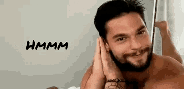 a shirtless man with a beard is laying on his stomach on a bed and smiling at the camera .