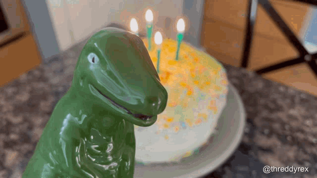 a green dinosaur stands in front of a cake with candles