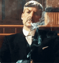 a man in a suit and tie is smoking a cigarette while sitting at a table .