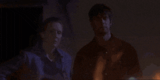 a man and a woman are standing in a dark room looking at a fire