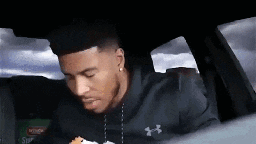 a man is sitting in the back seat of a car eating a burger .