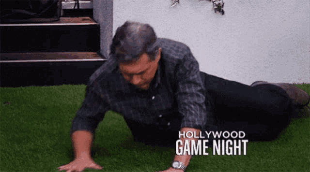 a man is doing push ups on the grass during a hollywood game night show .