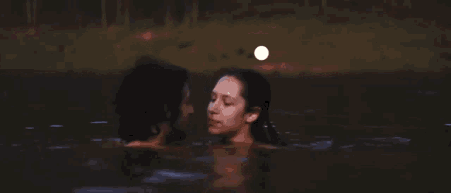 a man and a woman kissing in the water at night