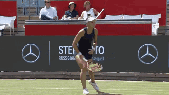 a woman is holding a tennis racquet in front of a mercedes banner