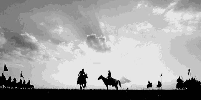 a black and white photo of people riding horses with flags in the background