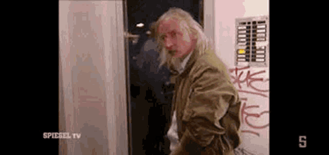 a man with long blonde hair is standing in front of a door .