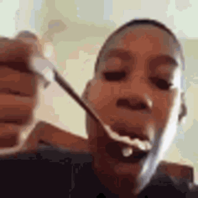 a young man is eating a spoonful of food .