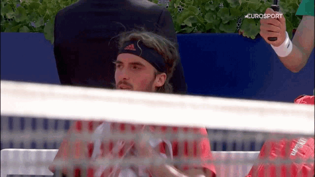 a man wearing an adidas headband is sitting on a tennis court .