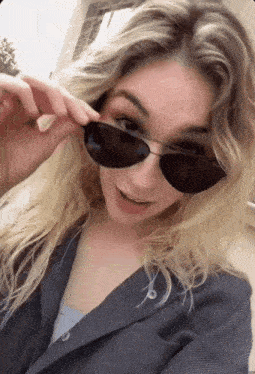a woman wearing sunglasses and a suit jacket looks at the camera
