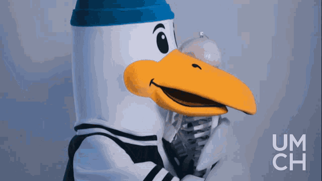 a mascot with a yellow beak is holding a microphone and the word um ch is on the bottom right