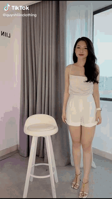 a woman is standing next to a white stool in front of a window and a sign that says tik tok