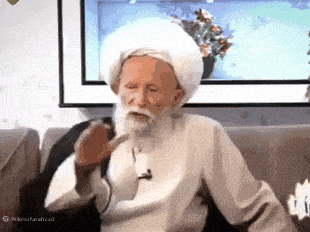 a man with a beard wearing a white turban is sitting on a couch .