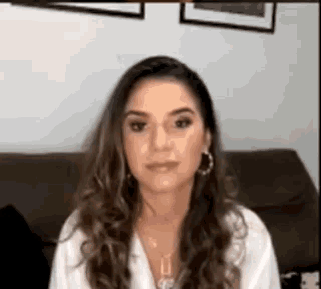 a woman is sitting on a couch wearing a white shirt and hoop earrings .