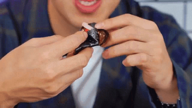 a man in a plaid shirt is eating a piece of chocolate .