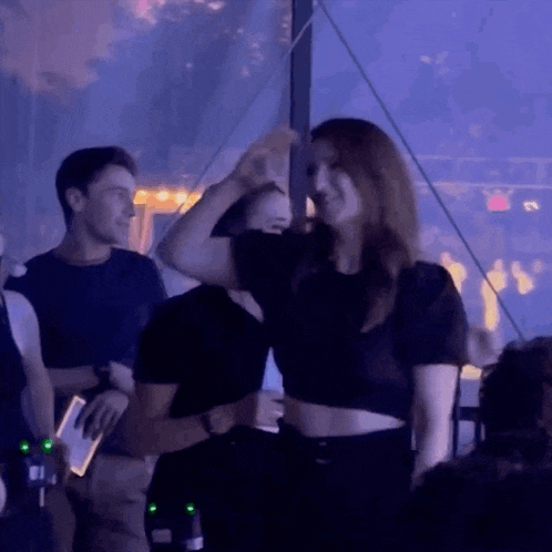 a woman in a black crop top is dancing in a dark room
